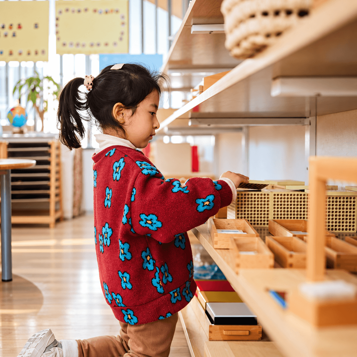 A child choosing materials from a low shelf in the Children’s House