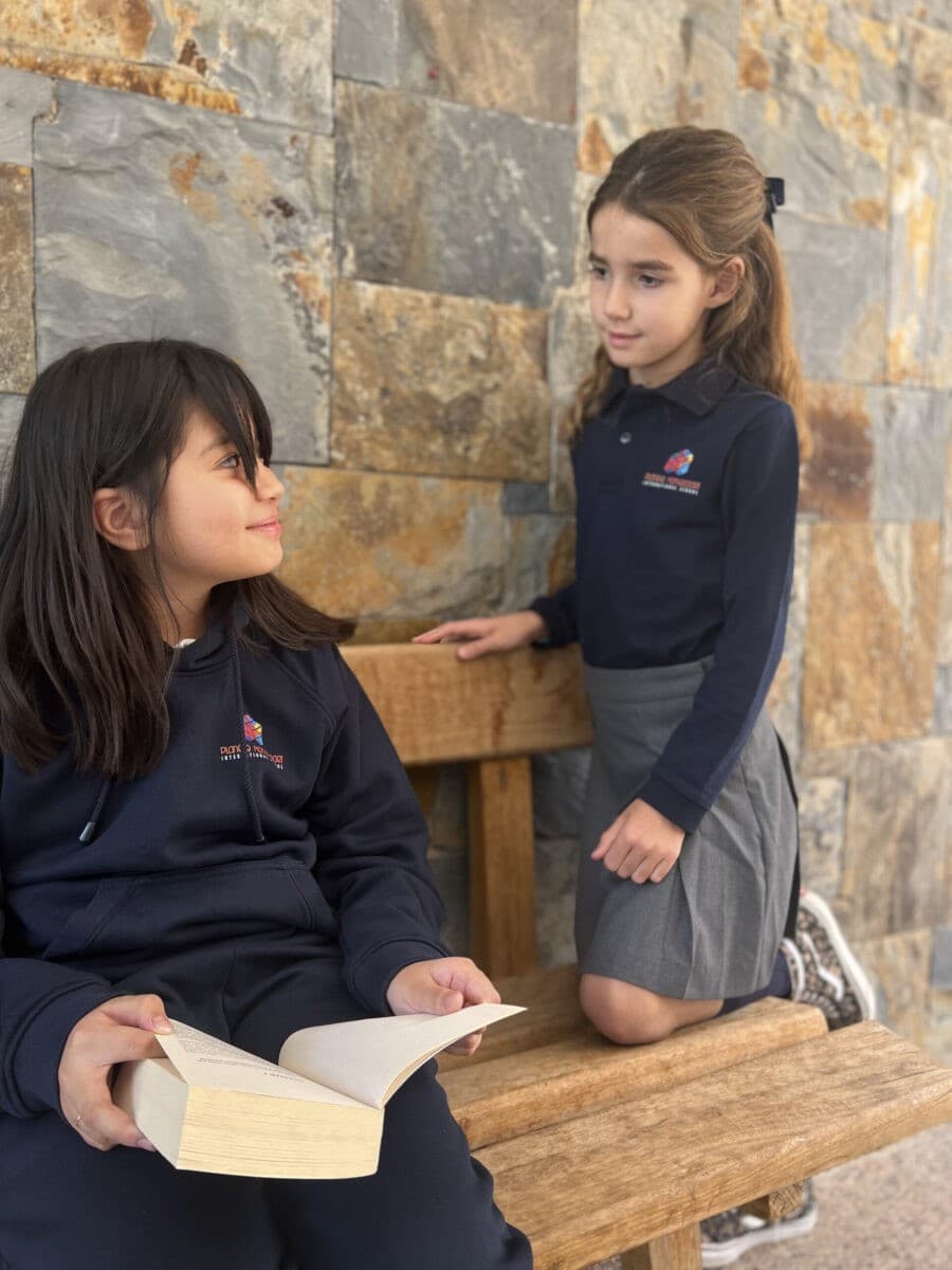 Two girls in navy uniform sitting on a bench with a book