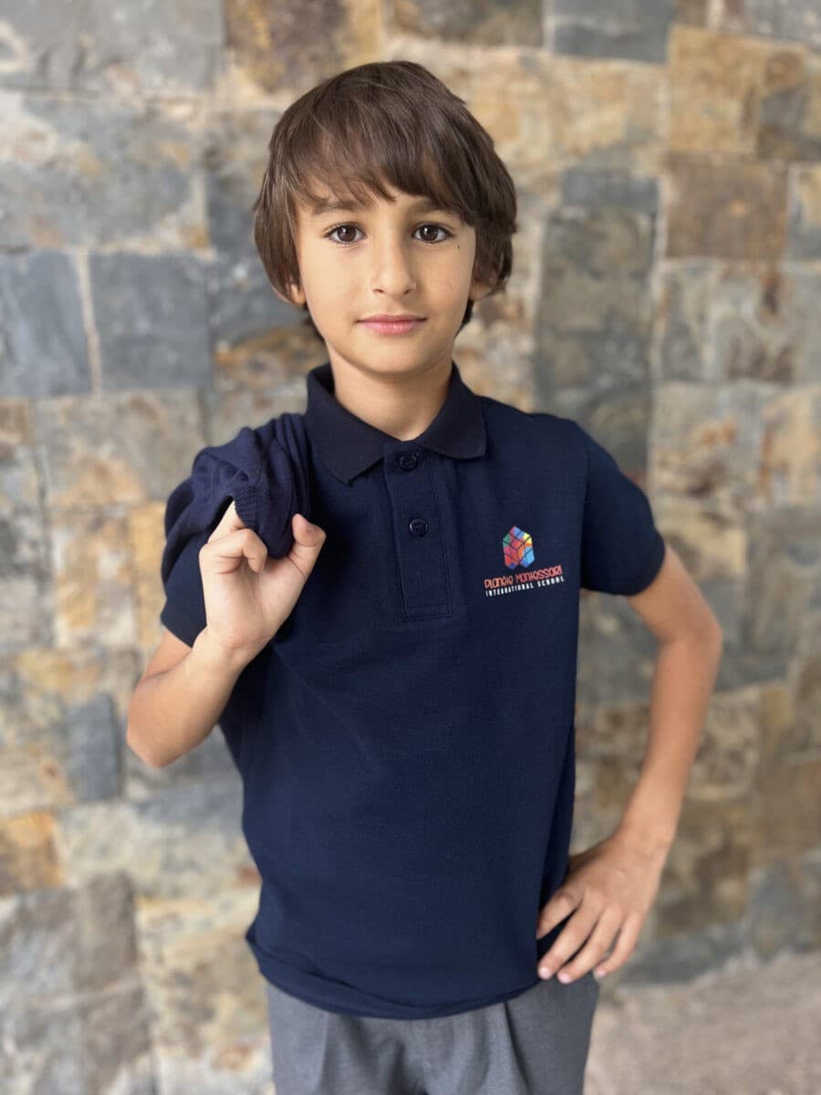 A boy in a navy school polo shirt and grey trousers
