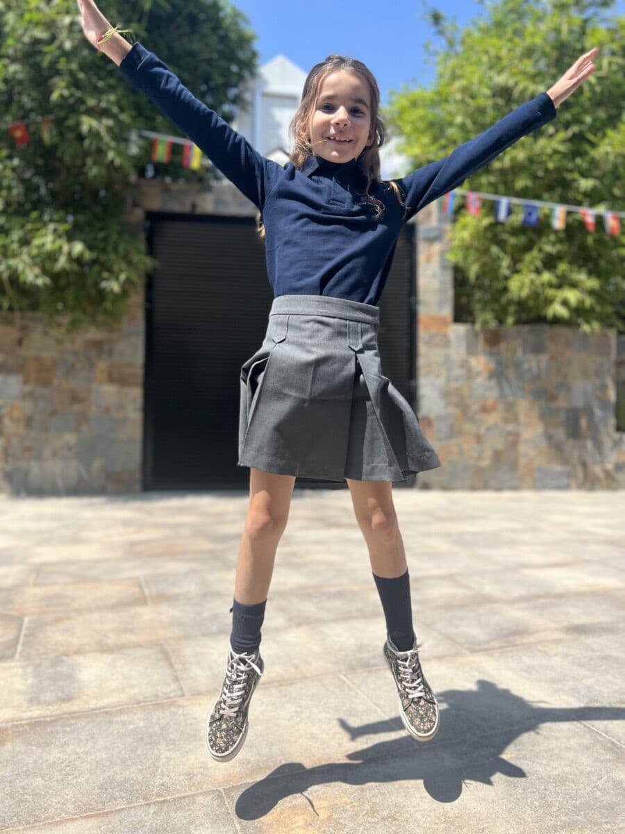 A girl in navy top and grey skirt jumping in the playground